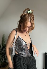 Srebrna majica sa šljokicama i asimetričnim dizajnom, uparena s crno-bijelim hlačama na pruge. Mala metalik torbica i svijetlozeleni scrunchie kao dodatak.