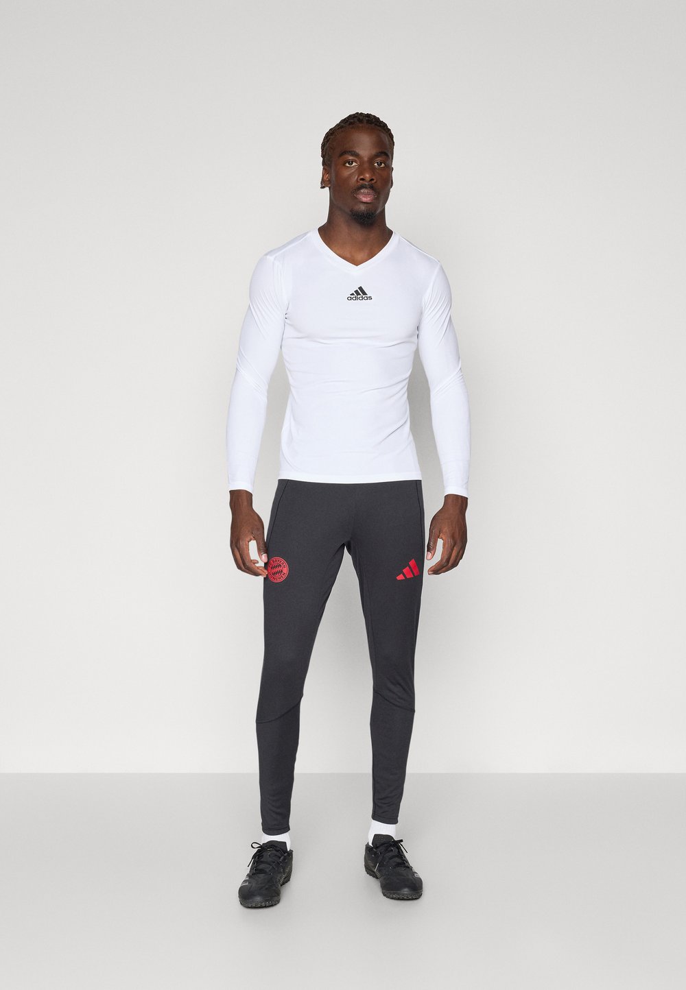 Balta garām piedurknēm sporta krekls ar melnu logotipu, kombinēts ar pielāgotām pelēkām biksēm ar sarkanu logotipu un svītrām, valkātas ar melnām kurpēm.