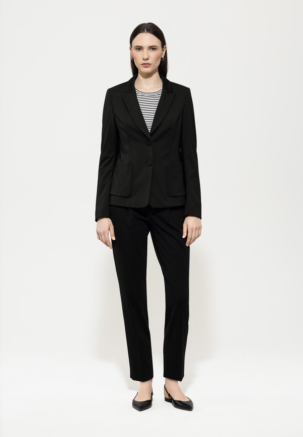 Black tailored blazer with two front pockets over a black and white striped top, paired with fitted black trousers and pointed-toe black heels.