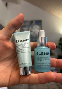 Dwa produkty do pielęgnacji skóry trzymane w ręce: krem ELEMIS Pro-Collagen Marine w srebrno-zielonej tubce oraz serum Pro-Collagen Future Restore w butelce w tym samym stylu.