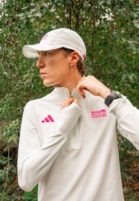 Light grey sports shirt with a half-zip, featuring the pink BMW Berlin Marathon logo and the Adidas logo. A white cap with ventilation holes.