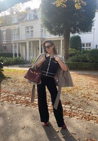 Μαύρο και λευκό πουκάμισο με γιακά, σε συνδυασμό με φαρδιά μαύρα παντελόνια. Γκρι κάπα ριγμένη στους ώμους και ένα μπορντό τσάντα.