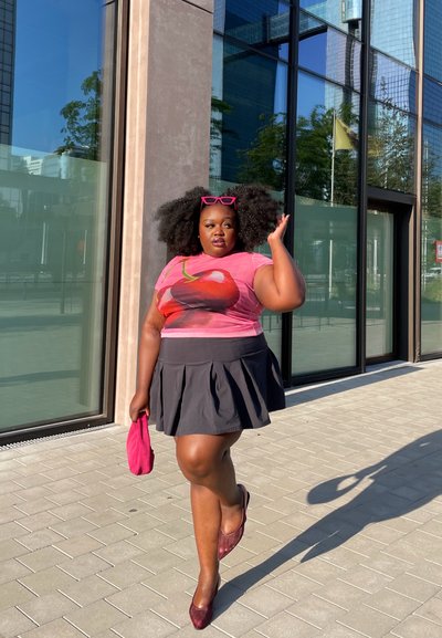 Camiseta gráfica rosa con diseño de cereza, combinada con una falda negra acampanada. Los accesorios incluyen gafas de sol rosas y un bolso a juego.