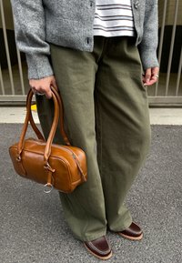 Braune Ledertasche mit doppelten Griffen, kombiniert mit olivgrünen weitem Hosenbeinen und dunkelbraunen Slippern mit Nahtdetails.