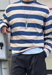 Kék és bézs csíkos, hosszú ujjú ing, mellzsebbel. Világoskék ing fölött viselve, sötét, textúrált nadrággal párosítva.