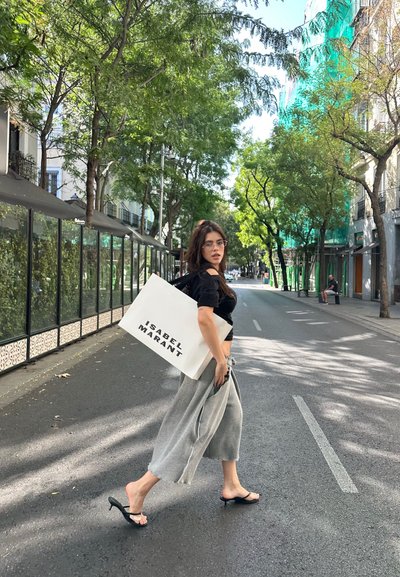 Modelo con un top negro recortado y pantalones de pierna ancha gris, llevando una gran bolsa blanca de mano con "ISABEL MARANT" impreso en letras negras en negrita.
