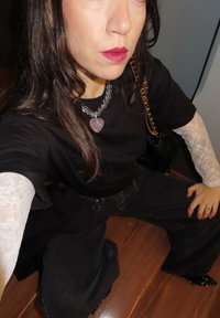 Zwart T-shirt en zwart hooggetailleerde spijkerbroek, mouwen van kant, hartvormige roze hanger, transparante ketting, en zwart gespen schoenwerk.