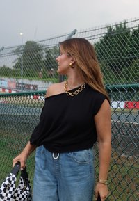 Μαύρη μπλούζα με έναν ώμο, ανοιχτό μπλε τζιν παντελόνι σε φαρδιά γραμμή, χρυσό χοντρό κολιέ και καρό τσάντα. Μακριά μαλλιά με ελάχιστα αξεσουάρ κοσμημάτων.