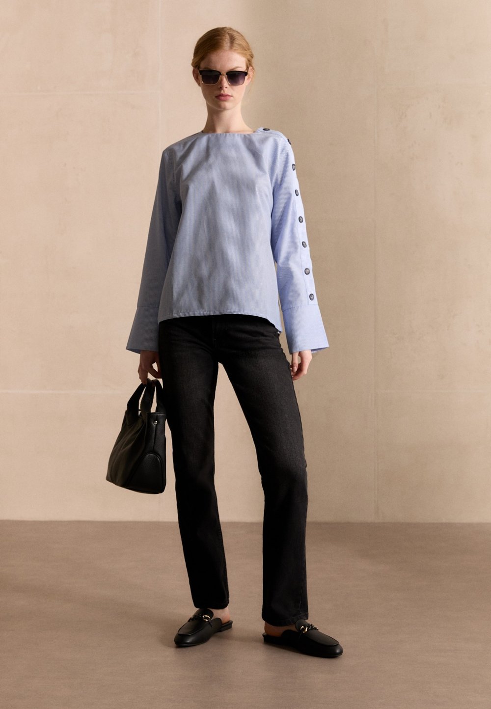 Helles, blaugraues Langarmhemd mit Knopfdetails, kombiniert mit schwarzen Jeans, schwarzen flachen Schuhen und einer schwarzen Handtasche. Glatte Textur, lockere Passform.