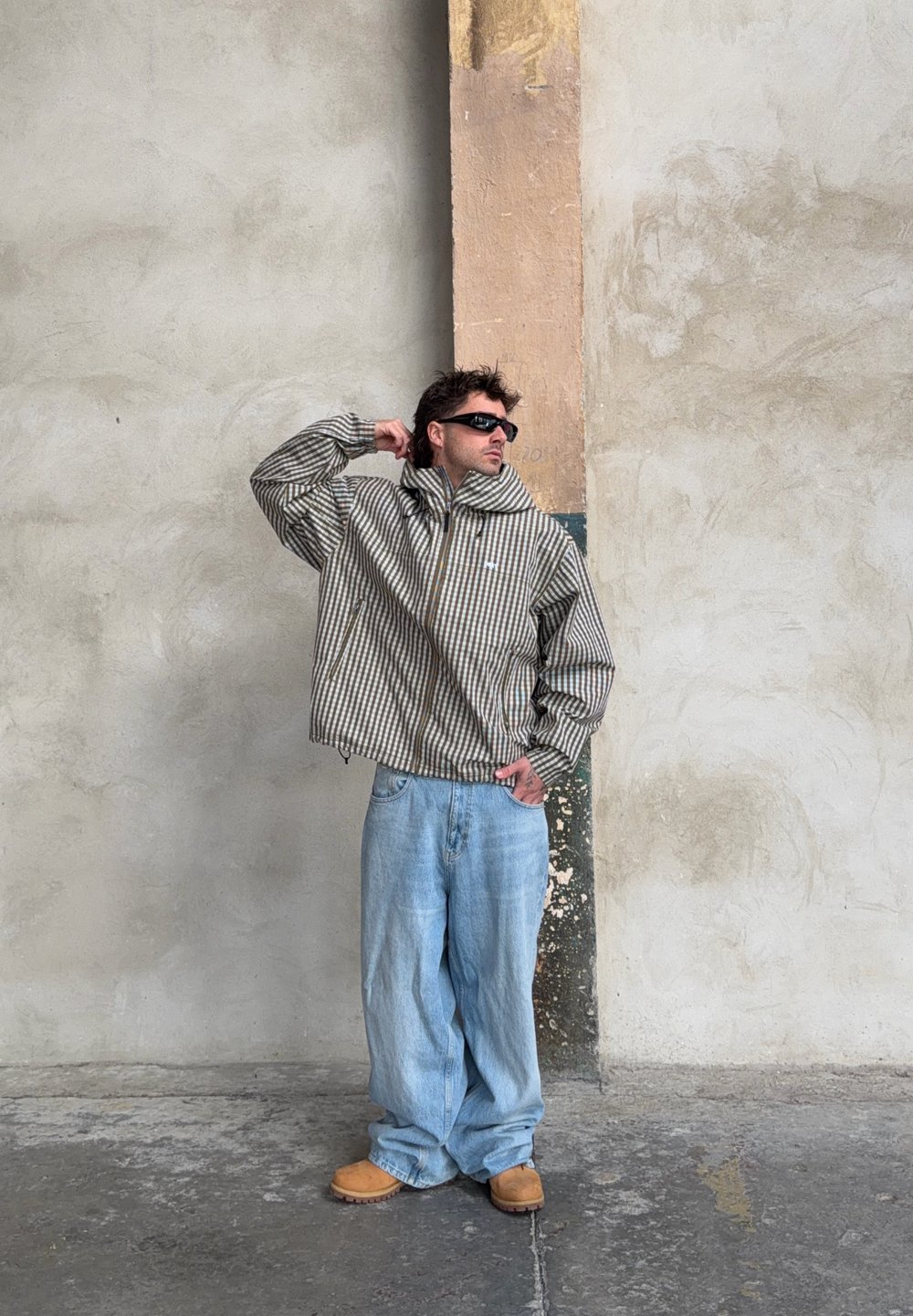 Dryžuota, per didelė ruda ir kreminė striukė, derinama su šviesiai mėlynomis laisvo kirpimo džinsais, rudais batais ir juodomis saulės akiniais. Tekstūruota medžiaga.