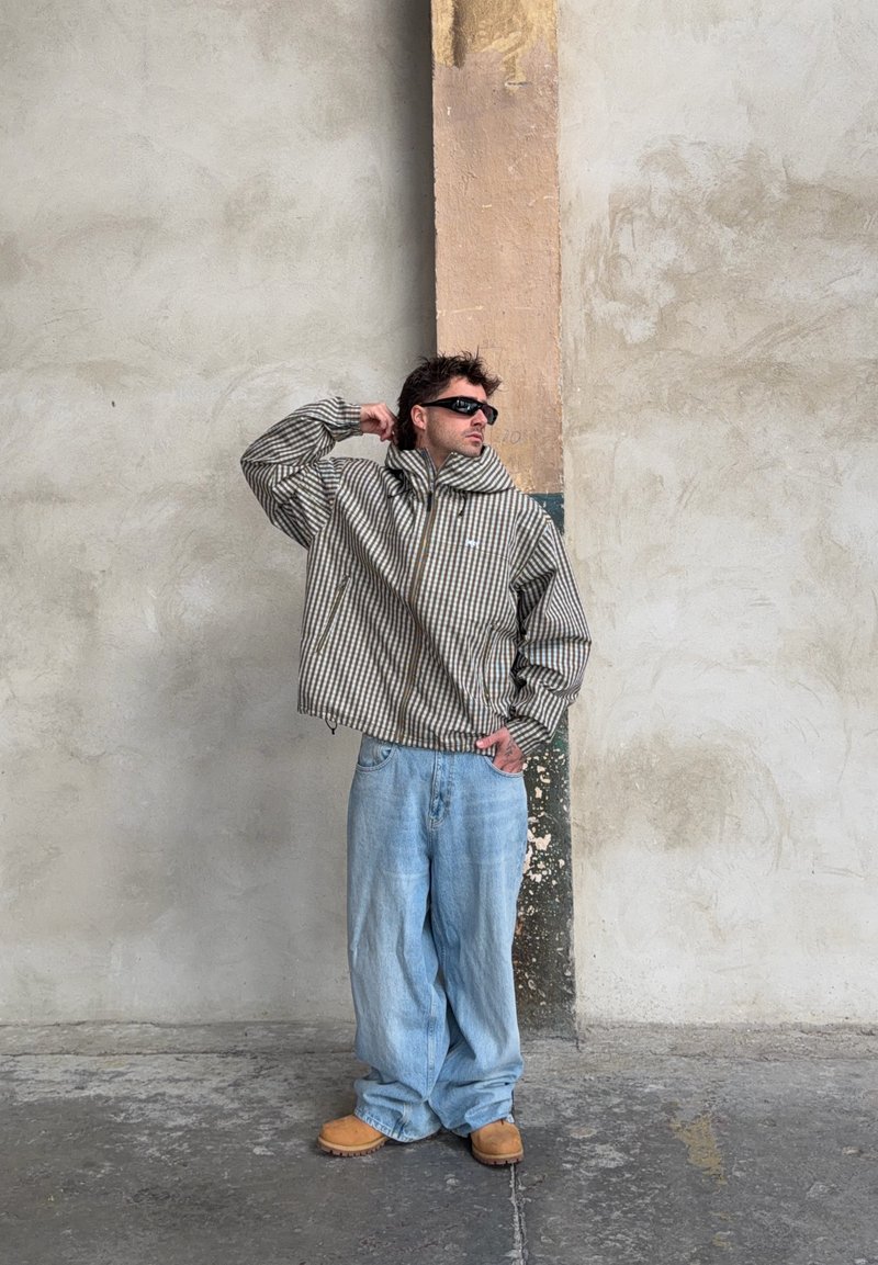 Gestreifte, übergroße Jacke in Braun und Creme, kombiniert mit hellblauen, weiten Jeans, braunen Schuhen und schwarzen Sonnenbrillen. Strukturierter Stoff.