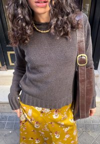 Pruun kootud kampsun soonikkoes äärega, mida kannab kollase lillemustrilise satiinse seeliku juurde. Pruun nahast kott on laia rihmaga ja messingist detailidega.