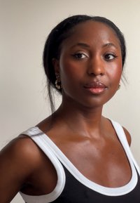 Czarny top na ramiączkach z białym wykończeniem, z dekoltem w serek. Czarne, długie włosy częściowo ułożone. Złote kolczyki koła dodają detalu. Naturalny kolor skóry.