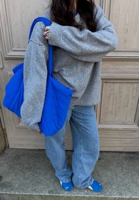 Pull gris en tricot, sac fourre-tout matelassé bleu ample, pantalon en denim bleu clair et chaussures bleues. Textures lisses avec une esthétique décontractée.