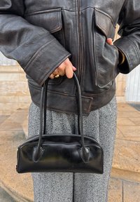 Schwarze Lederhandtasche mit zwei runden Griffen, Reißverschluss und eckigen Details. Kombiniert mit einem strukturierten grauen Hahnentrittmuster-Rock und einer schwarzen Lederjacke.