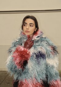 Bolyhos, túlságosan nagy kabát, amely többszínű, szakállas textúrákat mutat kék, piros, rózsaszín és fehér színekben, sötétbarna bőrkesztyűvel párosítva.