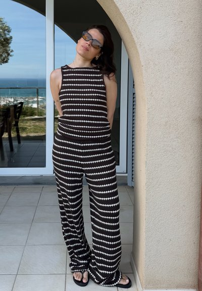 Mono de rayas en blanco y negro con piernas anchas y un cuerpo ajustado, confeccionado en tejido texturizado. Llevado con sandalias negras.