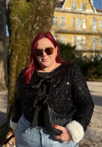 Cardigan en sequins noirs avec détail nœud, jean bleu clair et sac matelassé noir avec accents en fausse fourrure, porté avec des lunettes de soleil oversize.