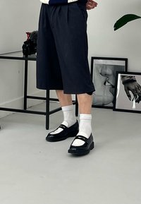 Zwarte leren schoenen met een witte neuskap, gedragen met witte sokken, gecombineerd met marineblauwe geplooide shorts met zijzakken.