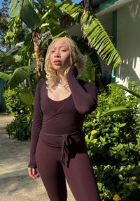 Body à manches longues, de couleur bordeaux foncé, avec un design portefeuille, incluant une ceinture à nouer à la taille et une texture côtelée, associé à des leggings assortis et ajustés.