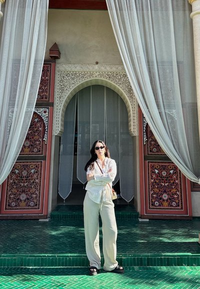 Una persona se encuentra frente a una puerta colorida y decorada con detalles ornamentales y cortinas transparentes, sobre una superficie de baldosas verdes con escalones.