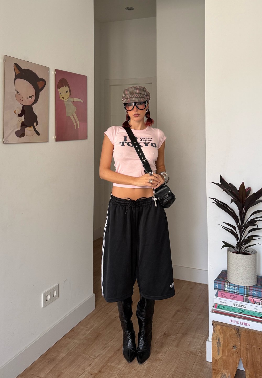 Pantaloni scurți atletici negri cu dungi albe, tricou roz scurt, cizme negre până la genunchi și o șapcă tip șoferailă în carouri. Geantă mică neagră.