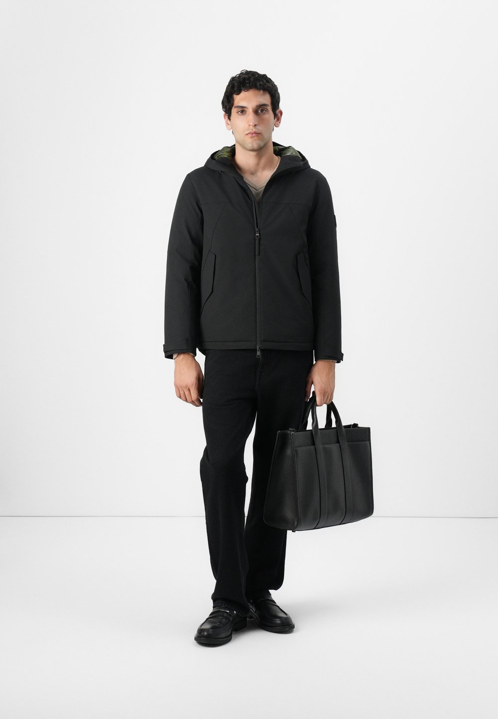 Μαύρο πουπουλένιο μπουφάν με κουκούλα, συνδυασμένο με σκούρες παντελόνες και μαύρη τσάντα. Το μπουφάν διαθέτει μπροστινό φερμουάρ και υφασμα με υφή.