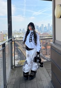 Black and white ensemble comprising oversized white trousers with rips, a white top adorned with black bows, and a small black handbag featuring a logo.