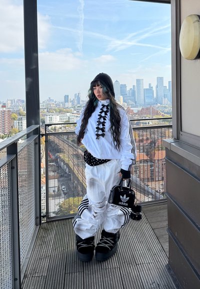 Conjunto en blanco y negro con pantalones blancos de gran tamaño que presentan desgarros, una blusa blanca con lazos negros y un pequeño bolso negro con logo.