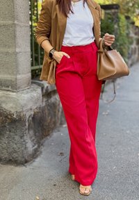 Blazer din suede bej, tricou alb, pantaloni largi roșu aprins și geantă maro. Sandale nude din piele lucioasă completează lookul.