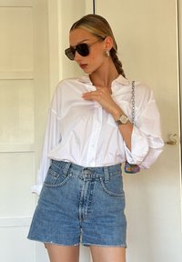Hvit skjorte med oppbrettede ermer, sammen med høy midje blå denimshorts. Tilbehør inkluderer solbriller og en perleveske.