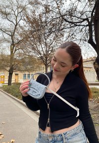 Μικρή ανοιχτό μπλε τσάντα χειρός με υφασμάτινη υφή, διαθέτει καμπύλη λαβή και αποσπώμενη λευκή όψη. Μινιμαλιστικός σχεδιασμός.