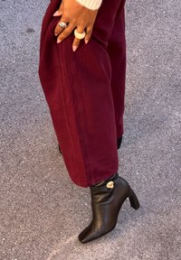 Zwarte leren enkellaarsjes met een vierkante neus en een blokhak, met een goudkleurig accent bij de enkel. Gecombineerd met bordeauxrode wijde broekspijpen.