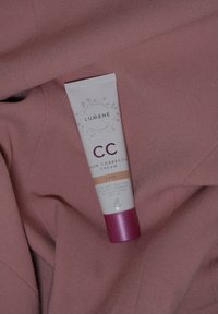 Lumene CC Color Correcting Cream i en tube med en lys rosa base og mørkere rosa hette, merket "Fair," som ligger på et mykt, rosa stoff.