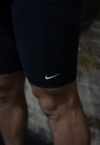 Μαύρες αθλητικές βερμούδες με στενή εφαρμογή, φτιαγμένες από λείο υλικό, διαθέτοντας πλαϊνή τσέπη και λευκό λογότυπο Nike στο στρίφωμα.