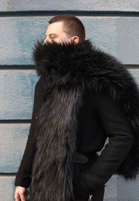 Écharpe en fourrure noire à texture longue et douce, portée sur un manteau sombre. Présente une couleur riche et profonde ainsi qu'une pleine épaisseur, encadrant le cou et les épaules.