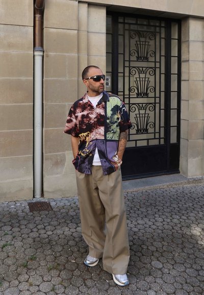 Camisa de manga corta estampada con una mezcla de colores que incluye burdeos y verde, combinada con pantalones beige holgados y zapatillas plateadas.