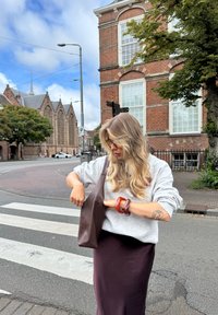Brązowa skórzana torba tote o luźnym fasonie, zestawiona z jasnoszarym, oversize'owym swetrem i ciemnofioletową spódnicą.