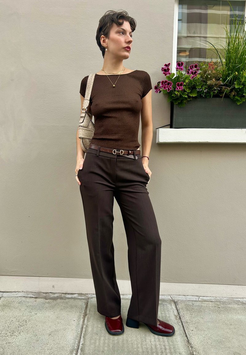 Καφέ ριγέ μπλούζα κοντού μανικιού, σκούρο καφέ φαρδύ παντελόνι, μπορντό παπούτσια με τετράγωνο τακούνι, ασημένιο κολιέ και μπεζ τσάντα ώμου.