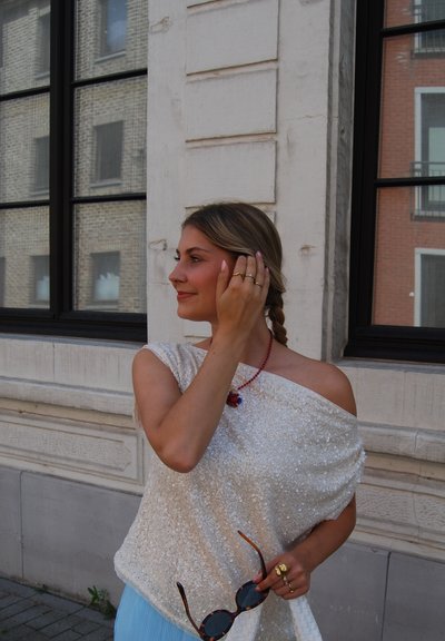 Top blanco con lentejuelas y estilo off-shoulder, combinado con una falda acanalada azul clara; llevando gafas de sol y un collar rojo.