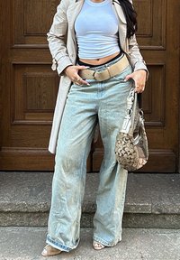 Jasnoniebieskie szerokie jeansy z wyblakłą teksturą, beżowy pasek, dopasowany jasny top oraz wzorzysty torebka na ramię, zestawione z sandałami na obcasie.