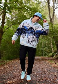 Fleece-pullovers med ljusblå bas, svarta och blå palmträd och tigermönster. Kombinerat med svarta cargobyxor och ljusblå sneakers.