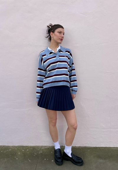 Camisa polo de manga larga a rayas en azul, blanco y granate, combinada con una falda plisada azul marino, calcetines blancos y mocasines negros.