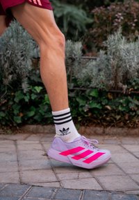 Hardloopschoenen in lichtpaars met felroze strepen, met een gestructureerd bovenwerk, gecombineerd met witte sokken met zwarte strepen.