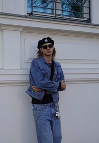 Denim jacket with a light blue wash, black shirt, light blue jeans, black beret with white logo, and sunglasses with silver chain detail.