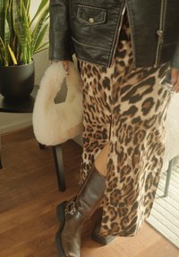 Brune lærstøvler til knæet, leopardmønstret maxiskørt, sort læderjakke, hvid fluffy håndtaske, indendørs omgivelser med grøn plante.