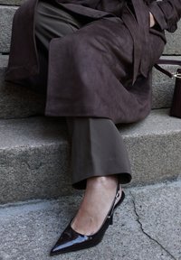 Smeđa suđena trench kaput preko maslinastozelenih hlača, uparen s sjajnim, tamnosmeđim slingback štiklama s uskim petama.