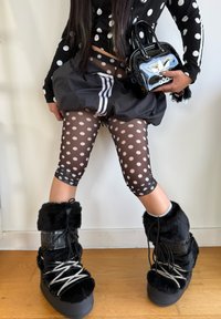 Musta lyhyt täplikäs paita, läpikuultavat täplikkäät leggingsit, kerroksittainen musta hame, mustat pörröiset nauhalliset saappaat ja kiiltävä musta minilaukku.