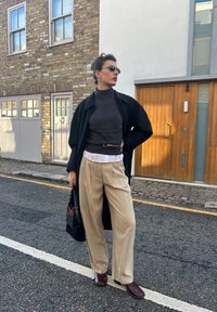 Svart lang frakk, mørkegrå turtleneck-genser, hvit skjorte under, beige plisserte bukser og burgunder tresko. Svart veske med burgunder detaljer.