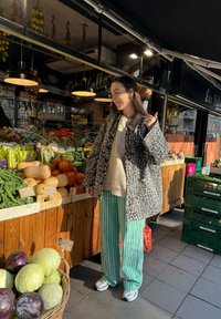 Handlekurvscene med en leopardmønstret frakk, grå genser og grønnstripete bukser. Omgitt av ferske produkter i kurver og kasser.